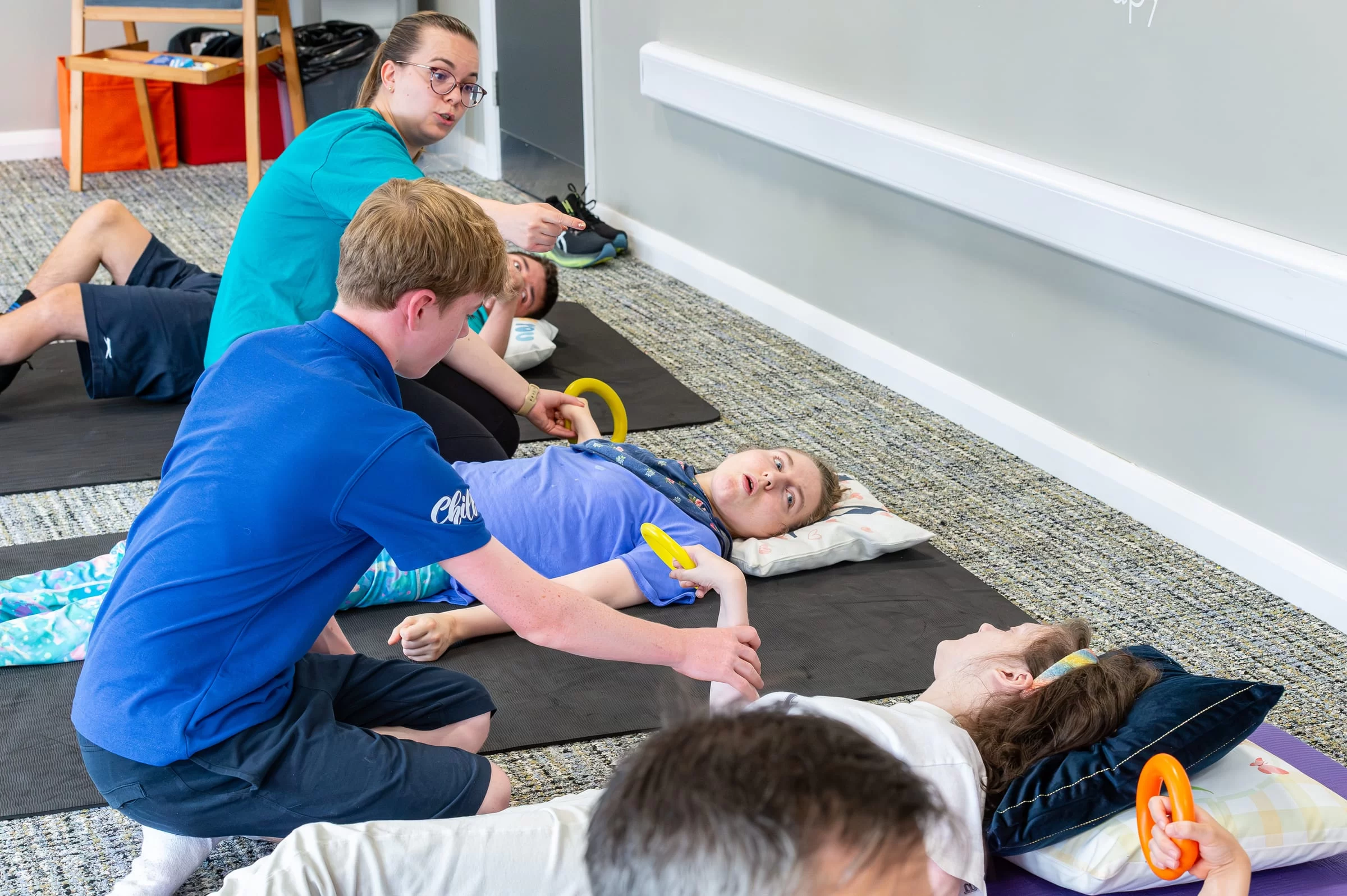 A therapist kneeling beside a young person on a mat, giving close hands-on support