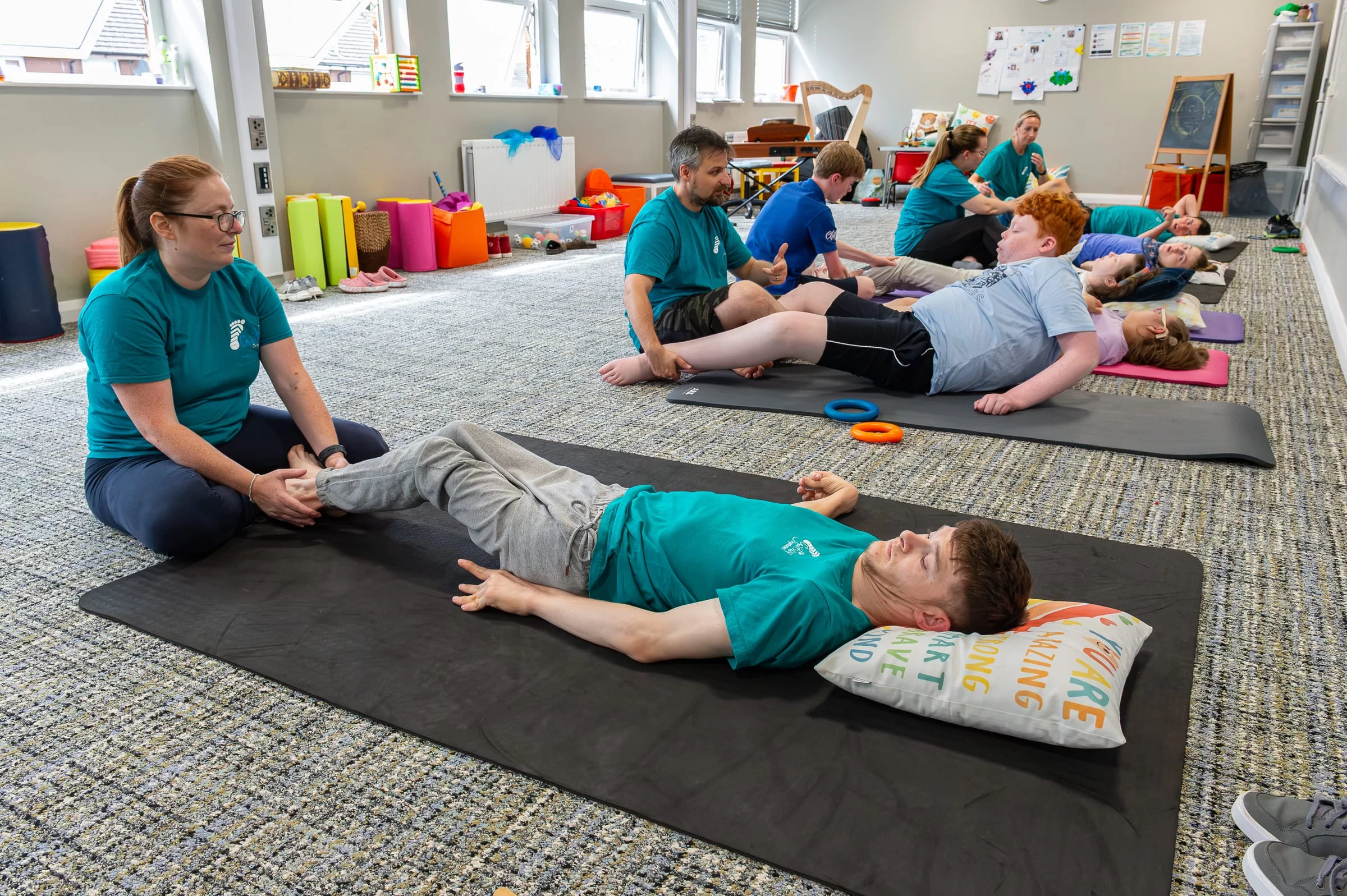 A full-length view of a therapist and a young person working through an exercise on a floor mat