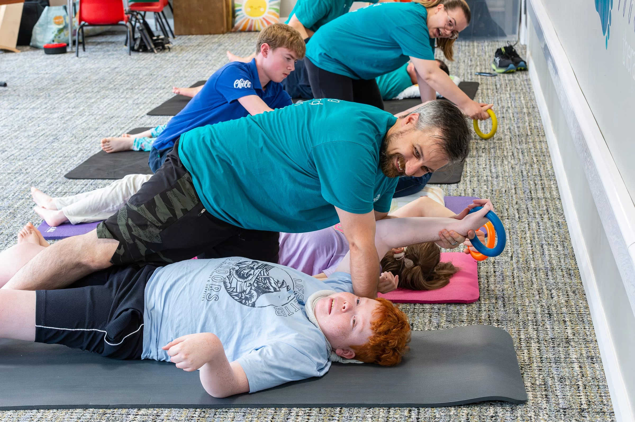 A therapist kneeling beside a mat, guiding a young person's arm movement