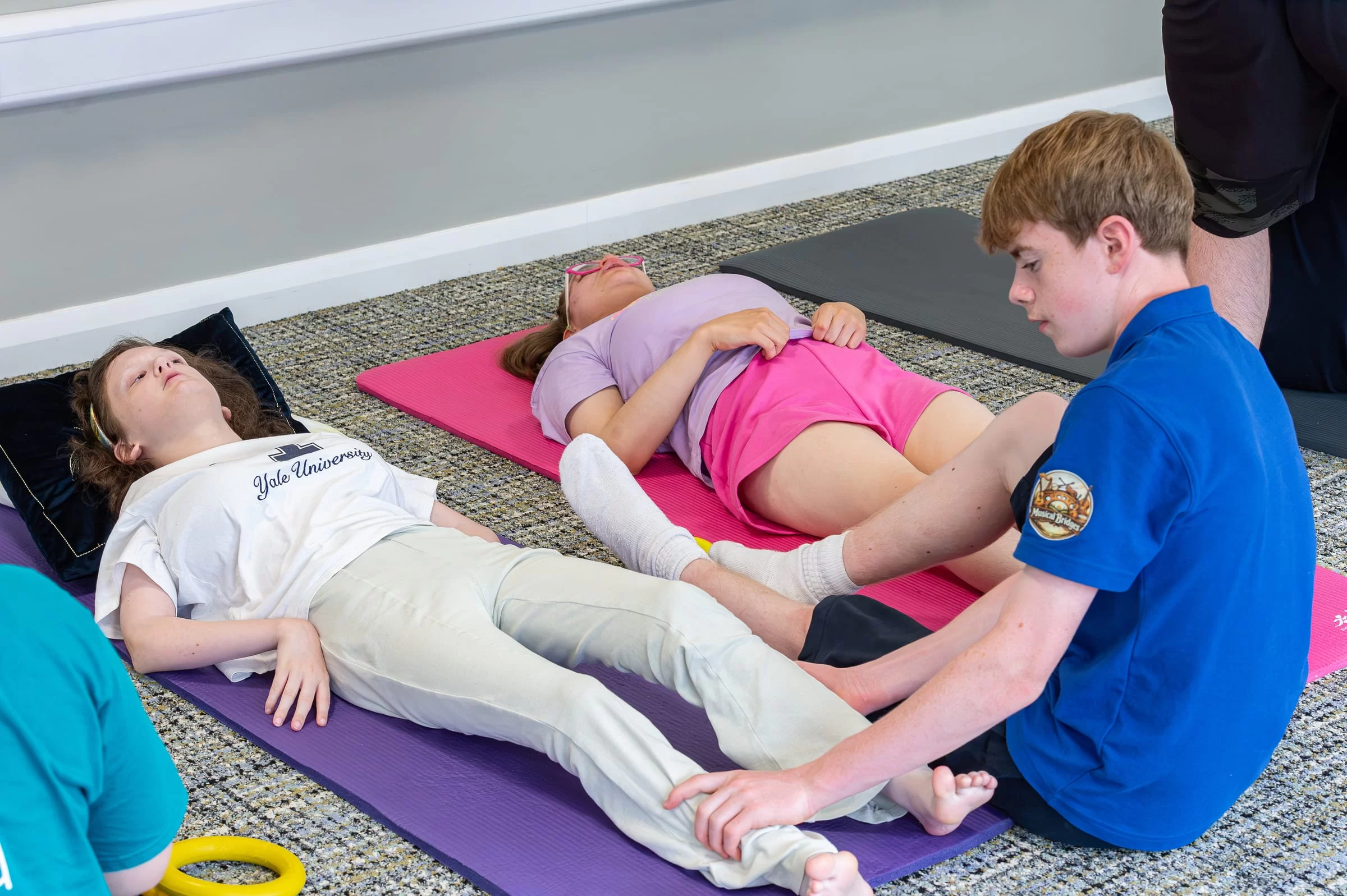A helper seated beside a young person on a mat during the senior group session