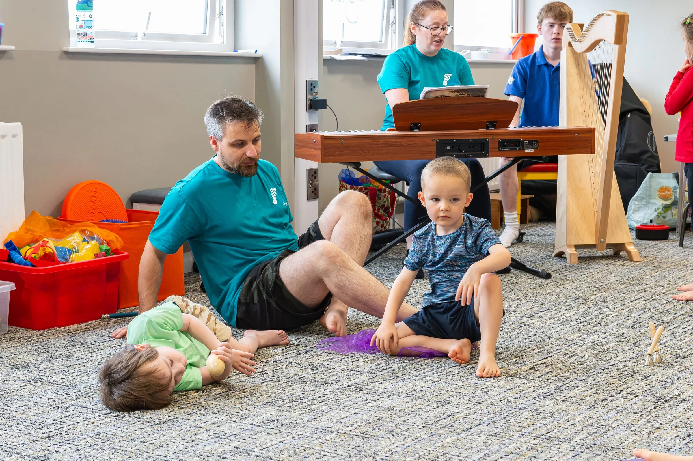 A therapist working with a child on a floor mat beside the keyboard during music therapy