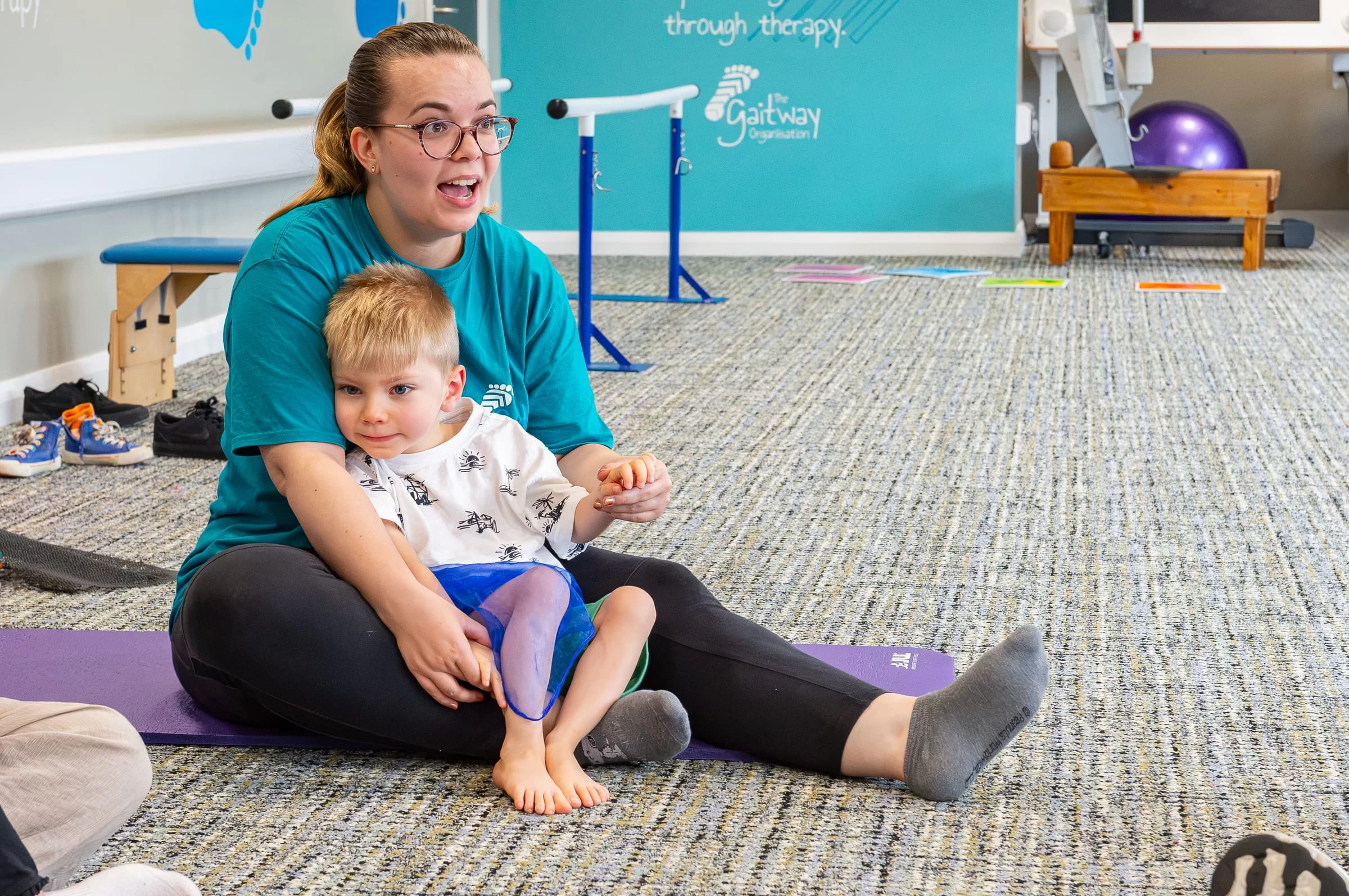 A therapist sitting on a mat with a toddler on her lap during a one-to-one session