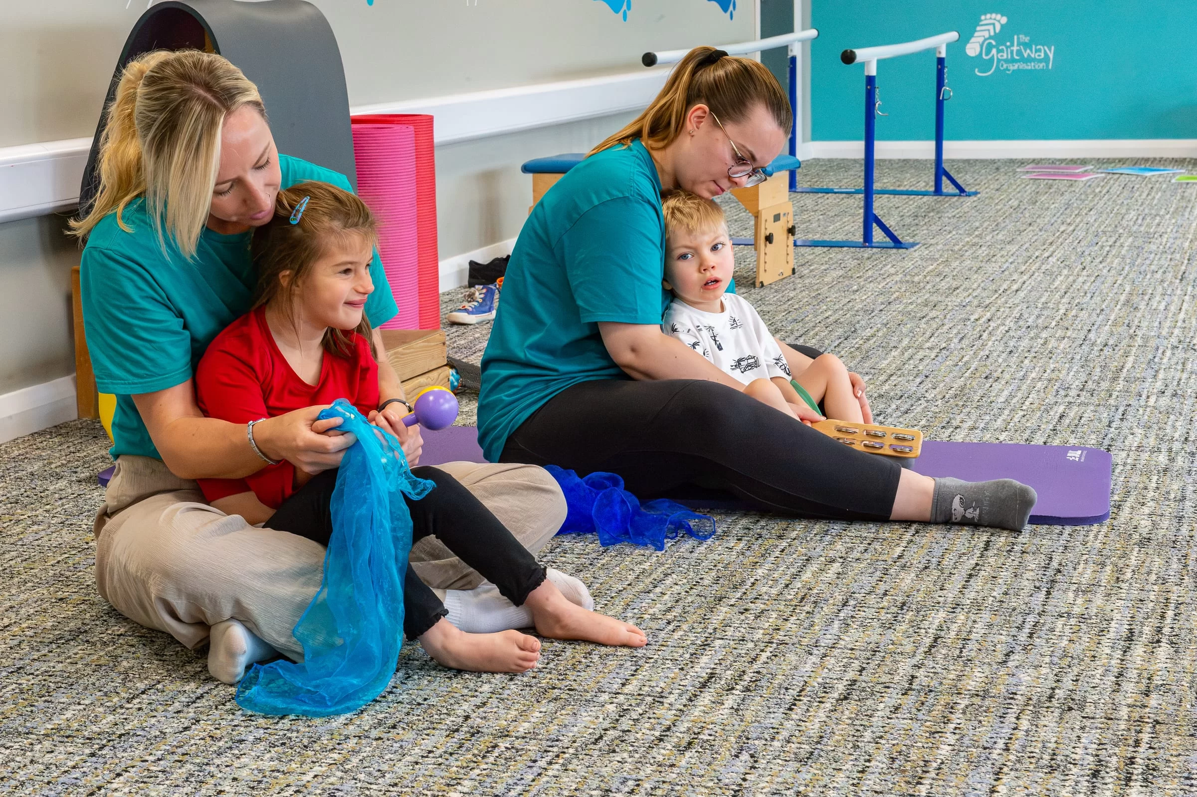 A young child reaching out towards a blue sensory scarf held by a therapist