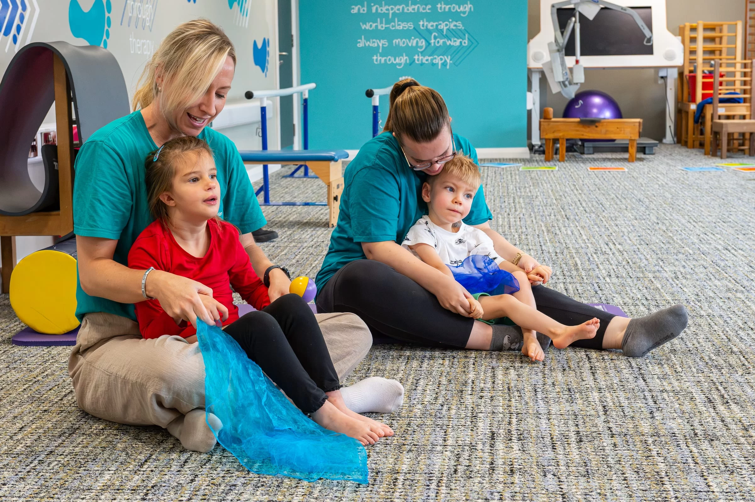 A child seated with support, playing with a length of blue fabric during a sensory activity