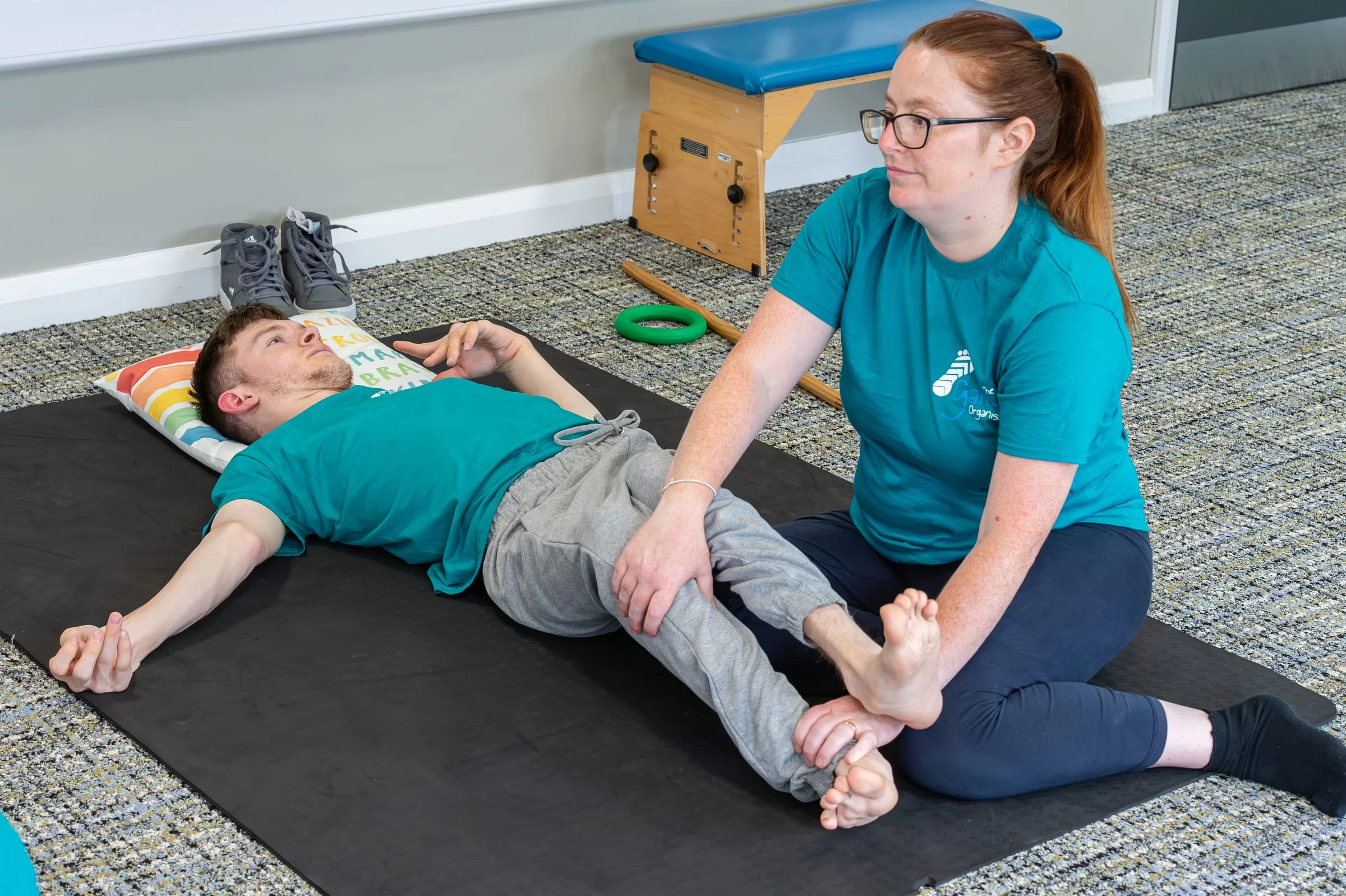 A therapist guiding a young person's leg through a controlled movement on a mat