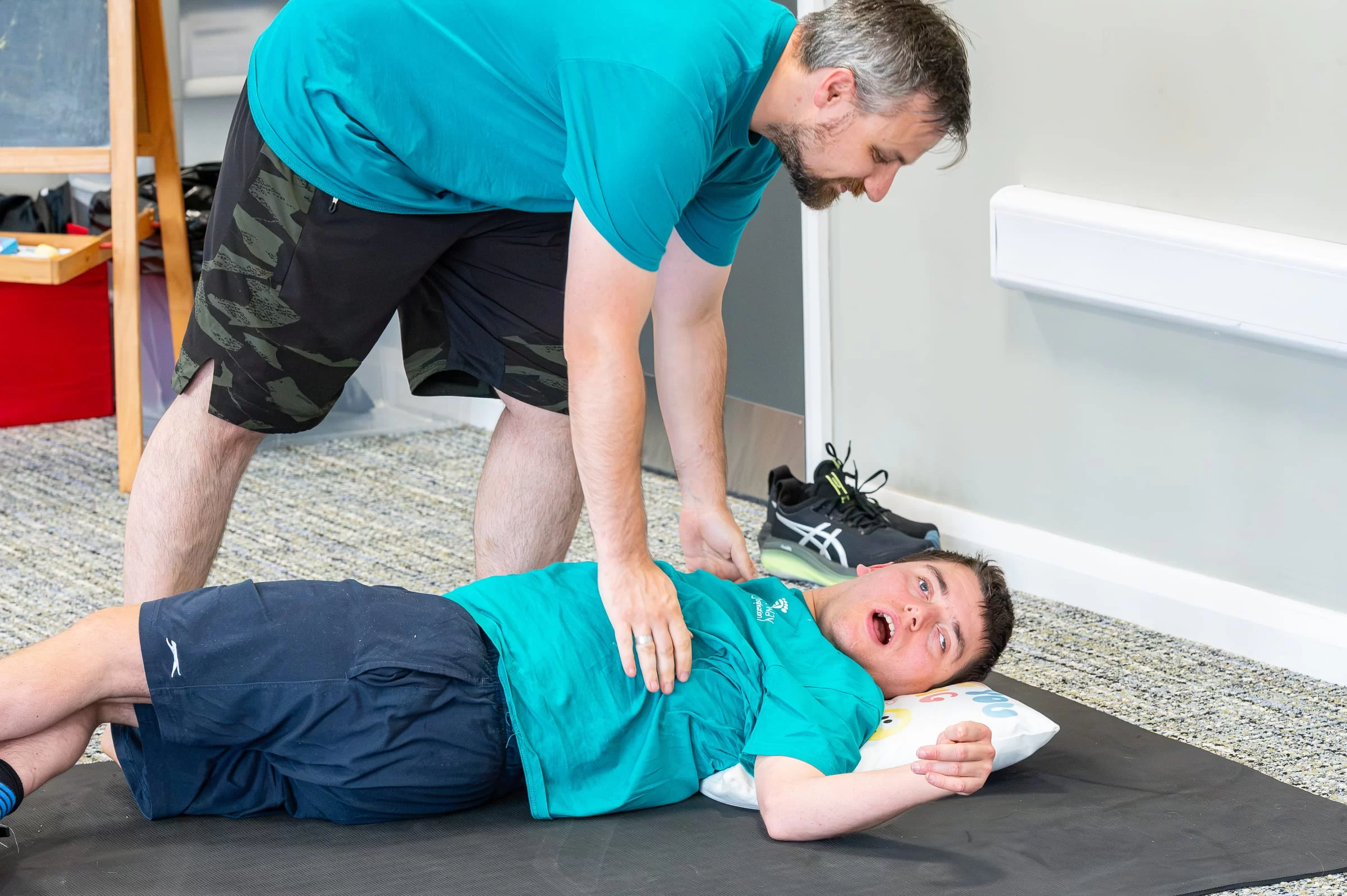 A therapist supporting an older child through a stretch while they lie on a mat