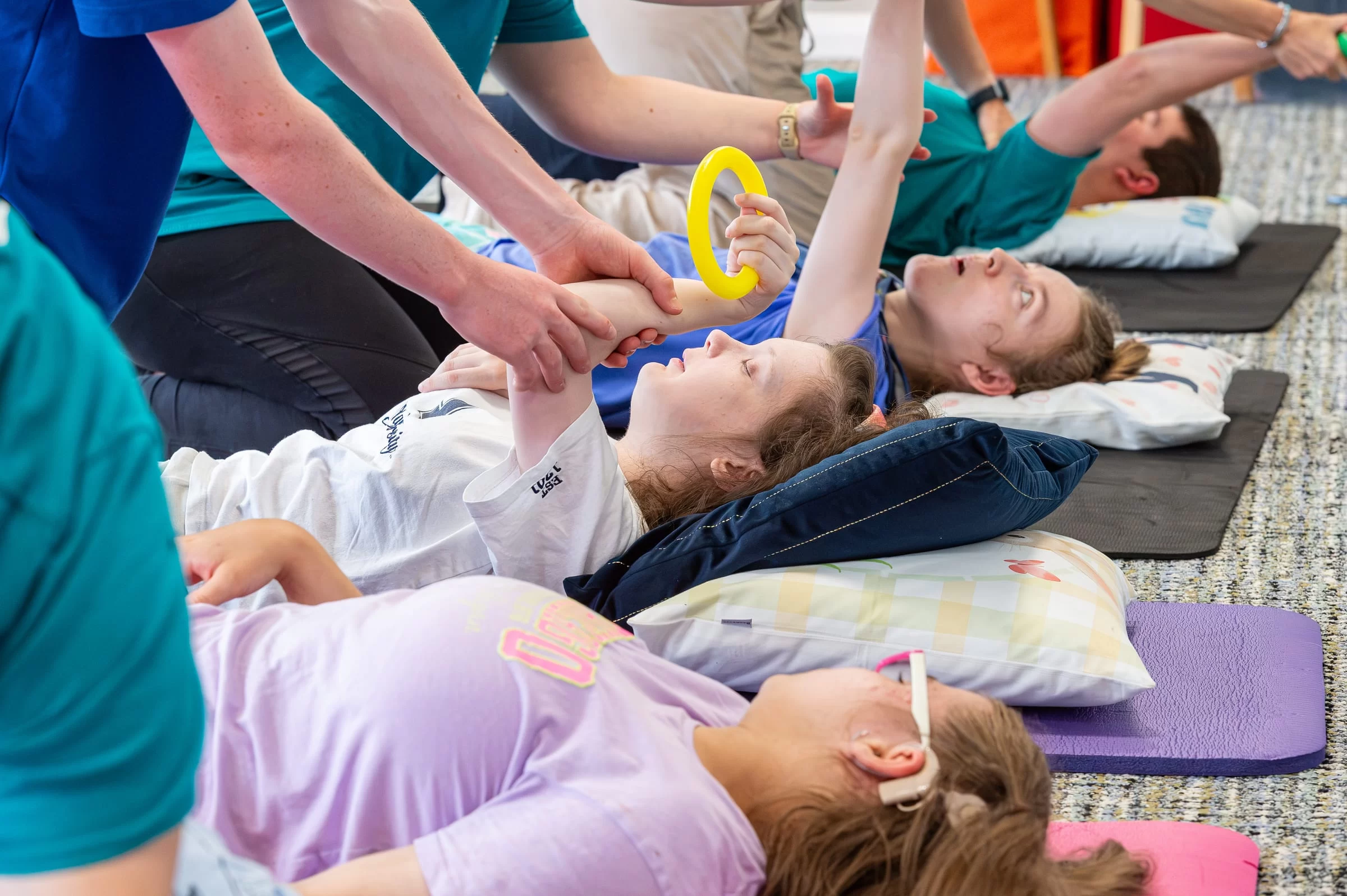 Hands guiding a young person's arm as they hold a yellow exercise ring