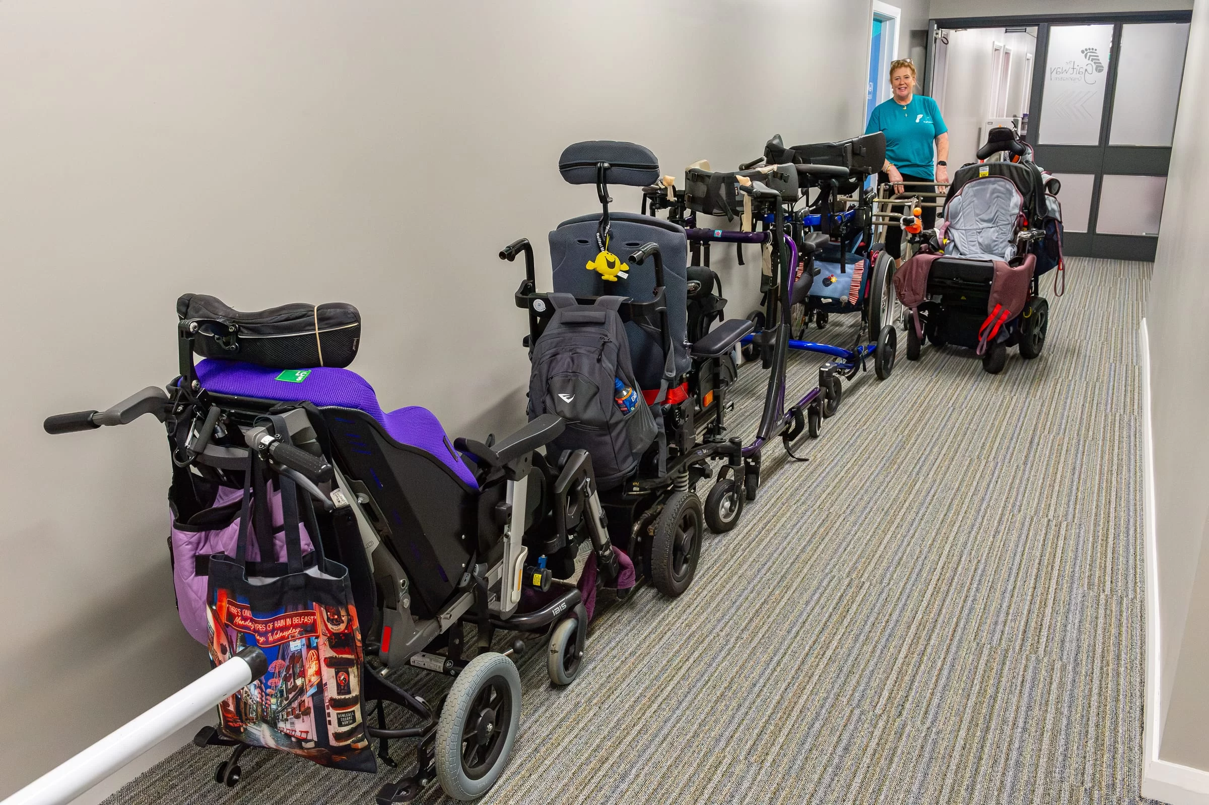 A row of wheelchairs and walking frames parked neatly along the wall inside the entrance