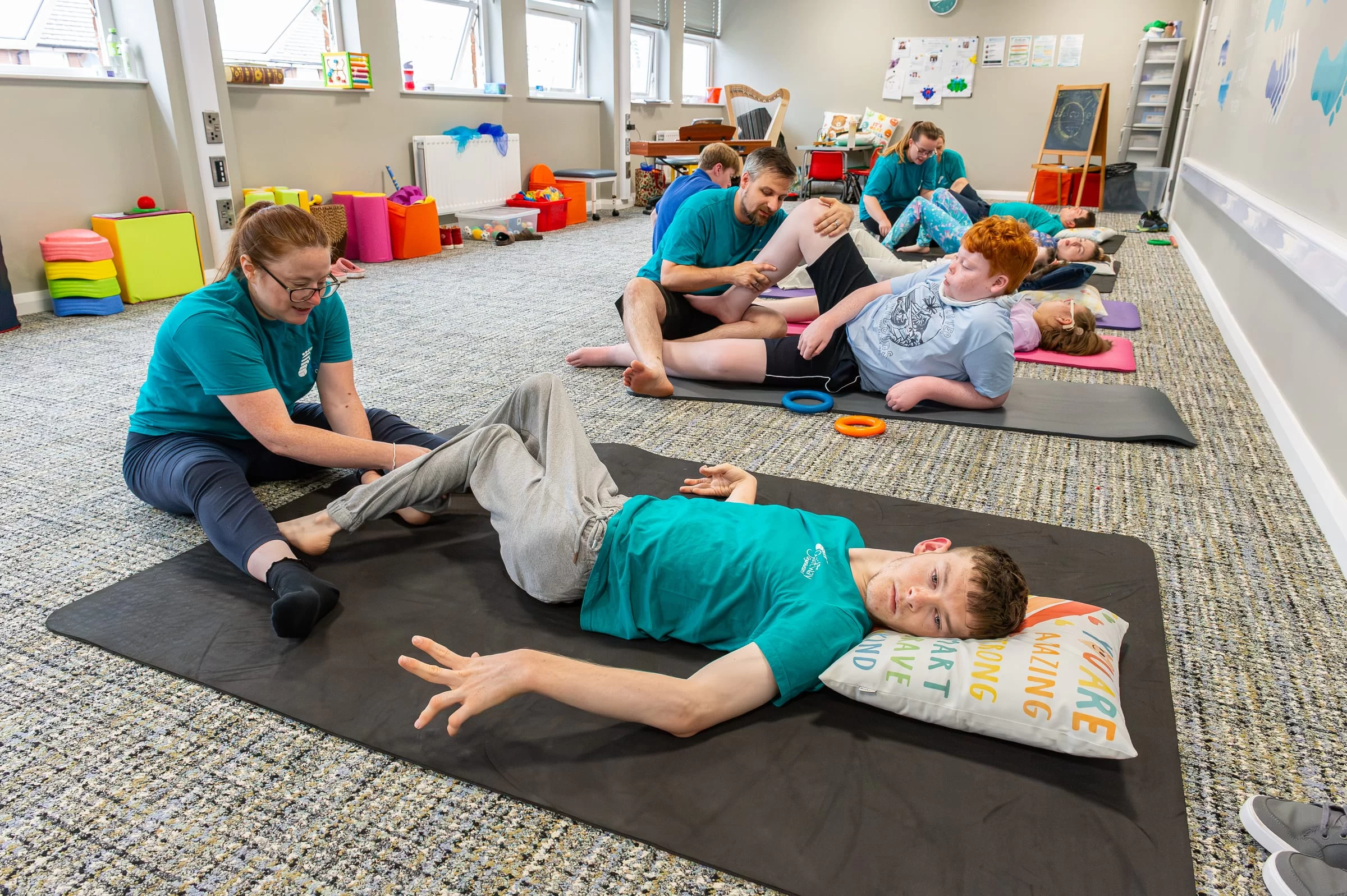 A therapist guiding a young person through a supported leg movement on a floor mat