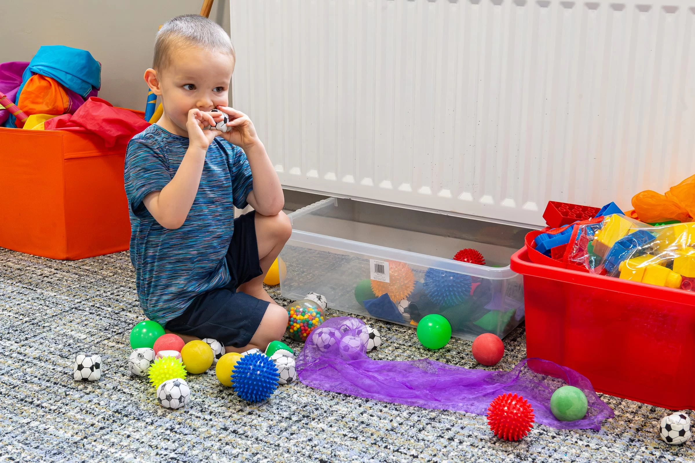 A young child sitting on the floor, concentrating as they choose from a set of coloured sensory balls