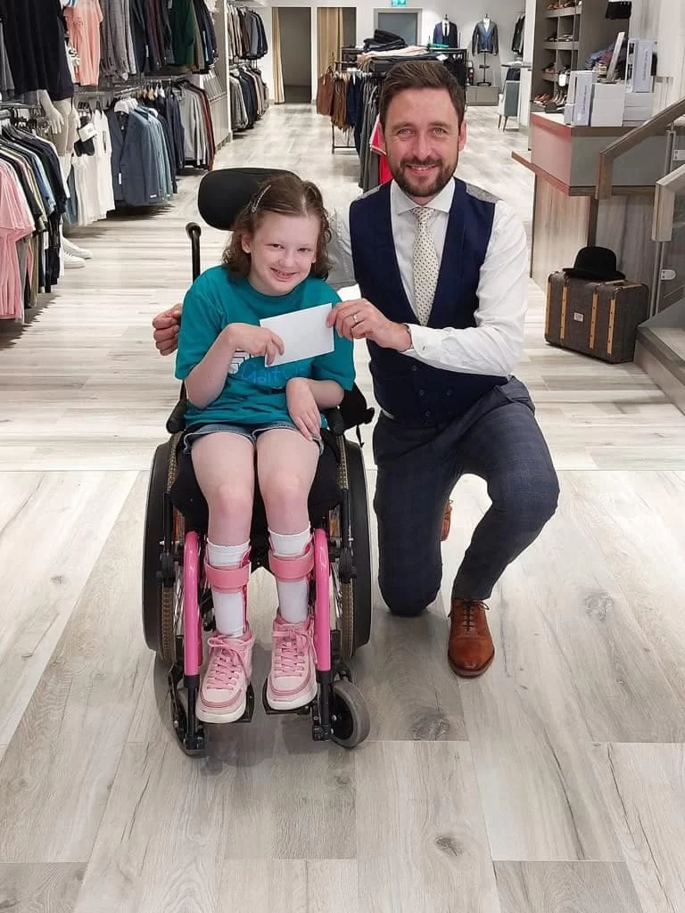 A young person in a wheelchair delivering a thank you card inside a local shop, with a member of staff kneeling alongside