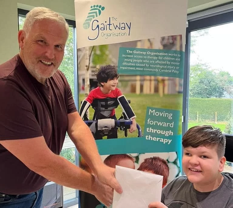 A young person handing a thank you card to a supporter beside a Gaitway banner
