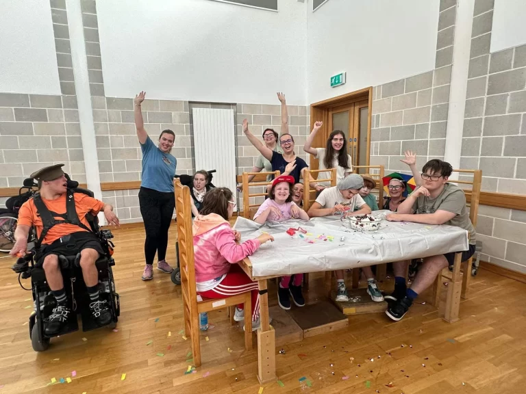 Children and staff around a craft table in the therapy room, several waving at the camera