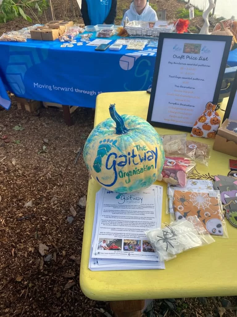 A pumpkin painted with The Gaitway Organisation's footprint logo, on a table of Gaitway leaflets, Halloween treat bags and the craft price list
